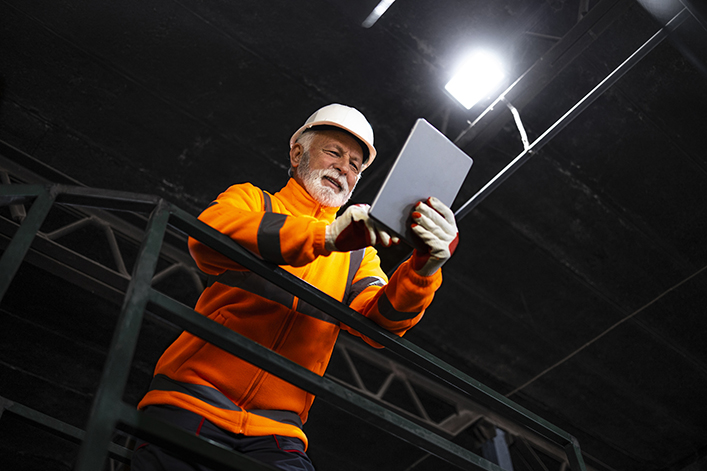 Portrait of miner in safety uniform, hardhat and lamp standing inside underground mine and checking ore production.